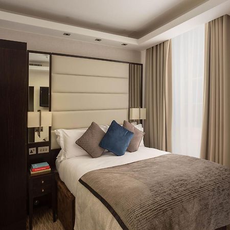Montcalm Brewery Townhouse Hotel London Exterior photo The image shows a cozy bedroom. It features a comfortable double bed with a light-colored duvet and decorative pillows in shades of blue and gray. The headboard is upholstered in a soft material, and there are bedside lamps on either side of the bed.
