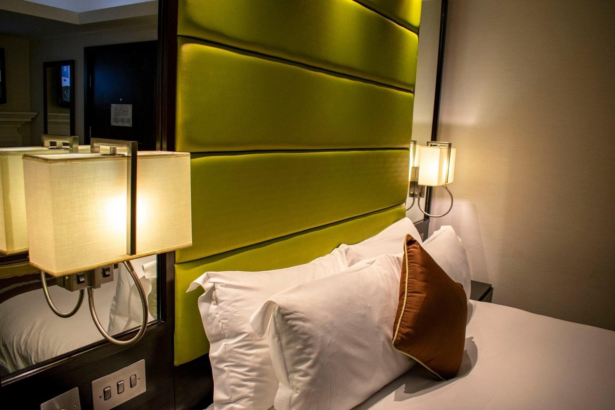 Montcalm Brewery Townhouse Hotel London Exterior photo The photo shows a modern hotel room with a stylish design. The focal point is a large bed with white pillows and a decorative brown pillow. The headboard is bright green and has a textured appearance. On either side of the bed, there are wall lamps t