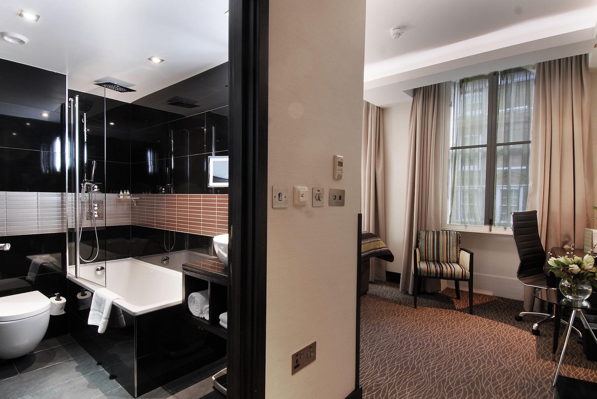 Montcalm Brewery Townhouse Hotel London Exterior photo The photo shows a modern hotel room that features an elegant bathroom on one side and a living area on the other. 

1. **Bathroom**: The bathroom is stylishly designed with a combination of black and white tiles. It includes a bathtub, a shower area 