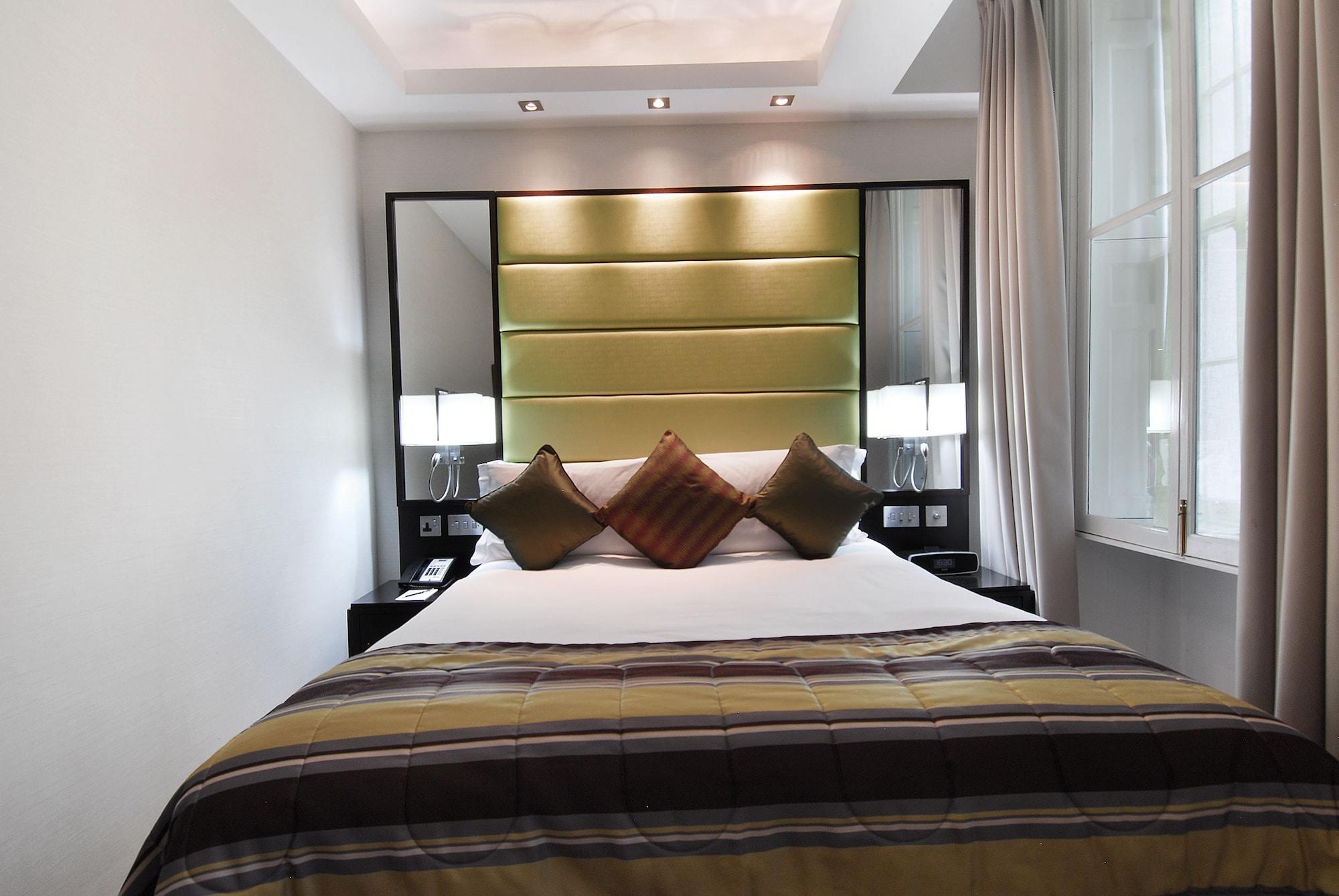 Montcalm Brewery Townhouse Hotel London Exterior photo The photo shows a stylishly decorated bedroom. The bed is centered in the room, featuring a white comforter with a plaid pattern in shades of brown and green. There are three decorative pillows on the bed, two in shades of brown and one in dark green