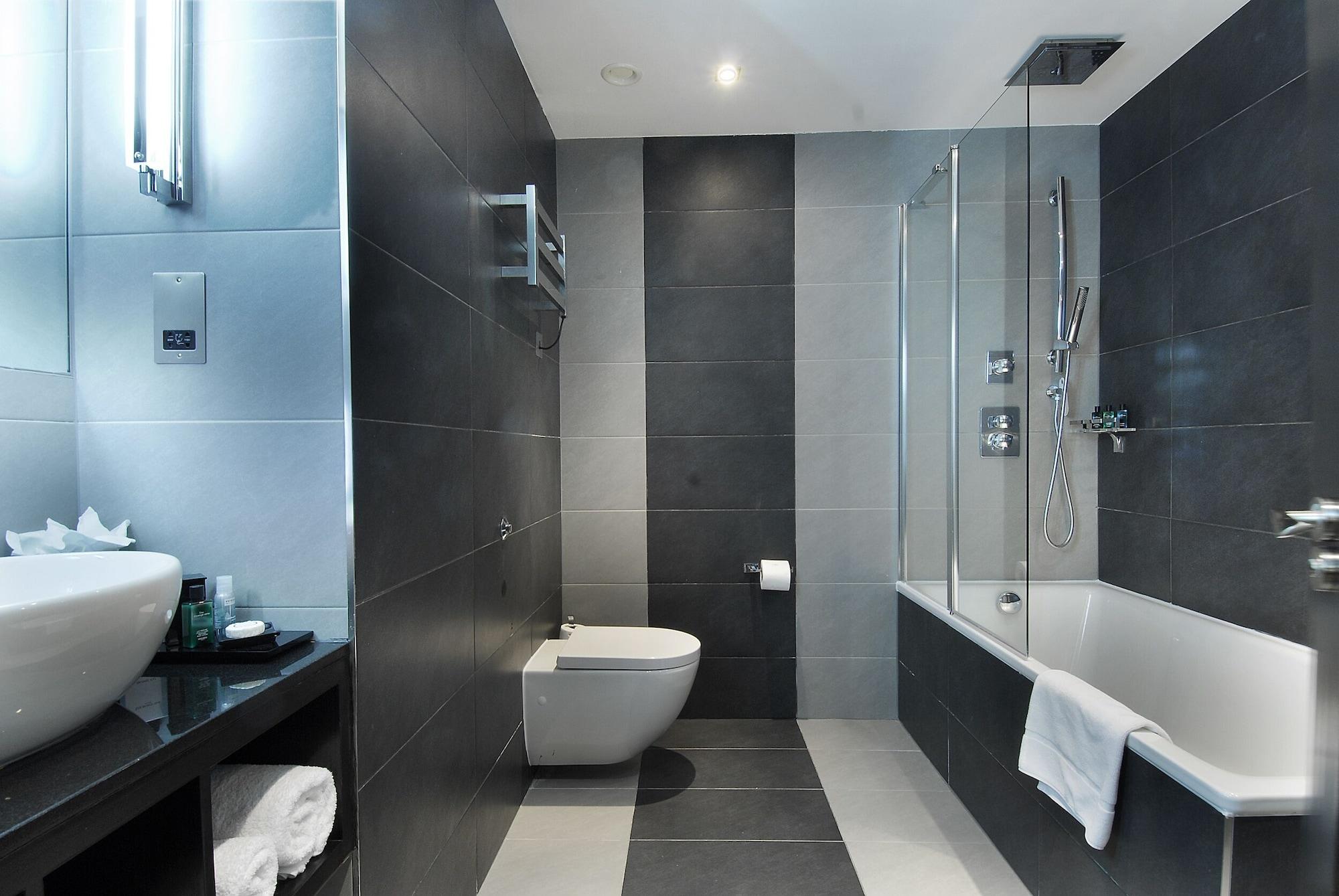 Montcalm Brewery Townhouse Hotel London Exterior photo The photo shows a modern bathroom featuring a sleek design. The walls are tiled in a combination of dark gray and light gray, creating a contemporary look. On the left, there is a countertop with a basin and some toiletries placed on it. The middle s