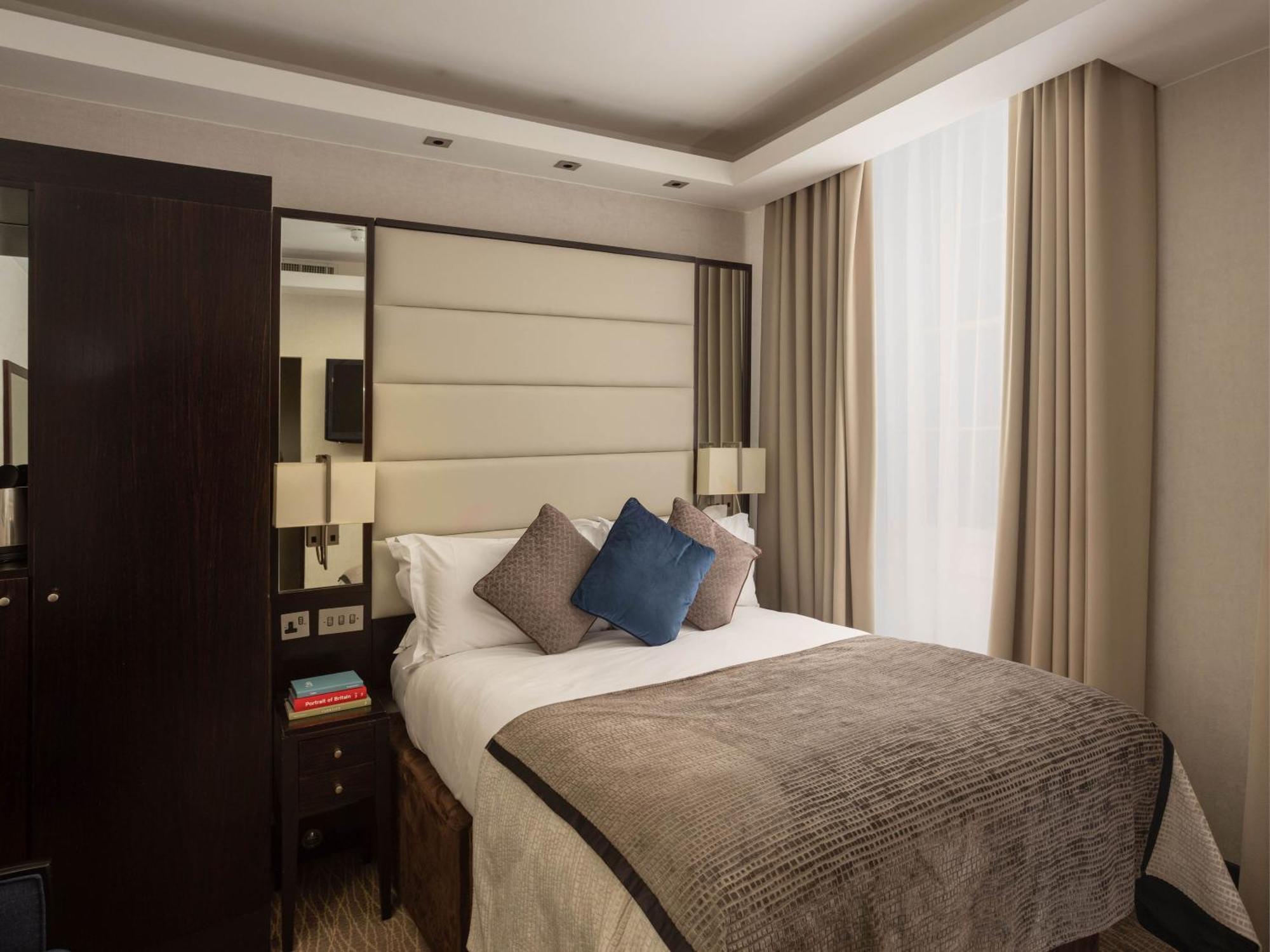 Montcalm Brewery Townhouse Hotel London Exterior photo The image shows a cozy bedroom. It features a comfortable double bed with a light-colored duvet and decorative pillows in shades of blue and gray. The headboard is upholstered in a soft material, and there are bedside lamps on either side of the bed.