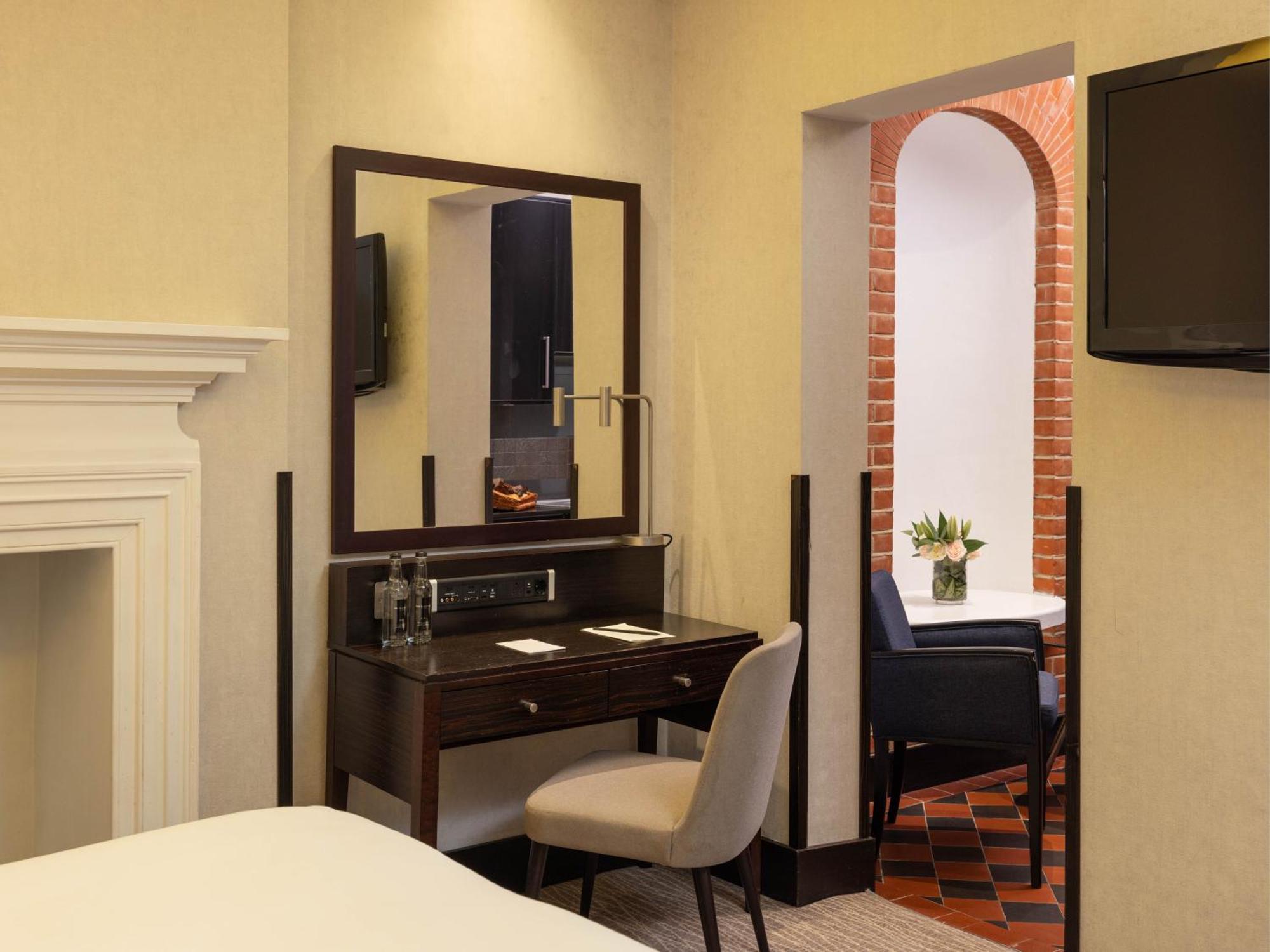 Montcalm Brewery Townhouse Hotel London Exterior photo The photo displays a hotel room setup. On the left side, there's a bed with a simple white bedding arrangement. Adjacent to the bed, there's a wooden desk with a chair, along with a mirror above the desk. The desk area is equipped with some glassware