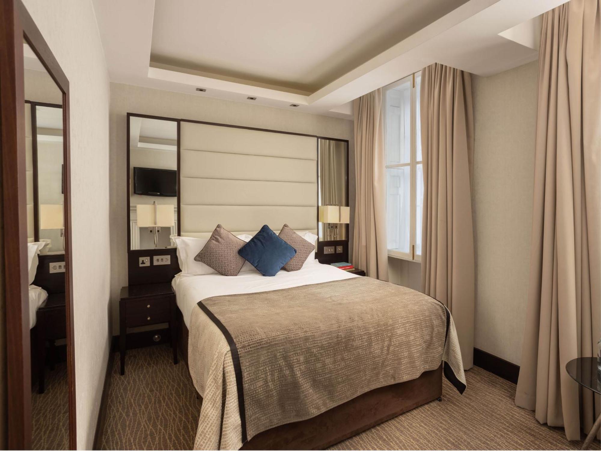 Montcalm Brewery Townhouse Hotel London Exterior photo The photo shows a cozy hotel room with a bed as the focal point. The bed is made with neutral-colored linens and has several pillows, including a decorative blue one. There are bedside tables on either side of the bed, each with a lamp. A large mirro