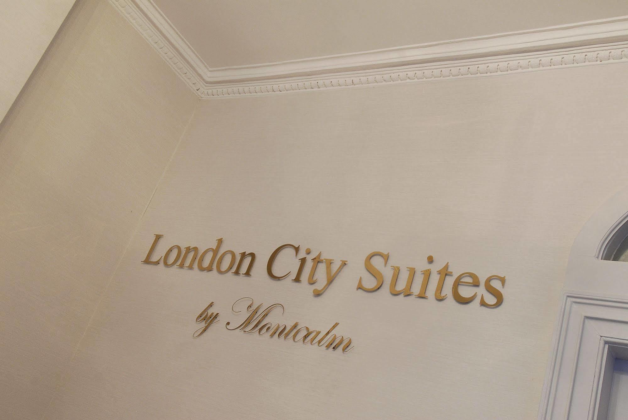 Montcalm Brewery Townhouse Hotel London Exterior photo The photo shows a wall display featuring the text "London City Suites" in a bold, gold-colored font. Below that, the words "by Montcalm" are written in a smaller, elegant style. The background appears to be a neutral-colored wall, possibly in a hotel