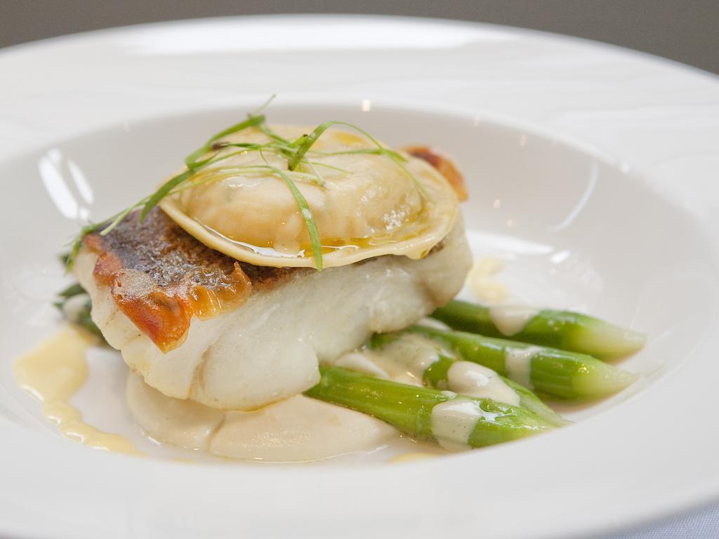 Montcalm Brewery Townhouse Hotel London Exterior photo The image shows a beautifully presented dish featuring a piece of fish, likely a white fish, topped with a clam. It is served on a bed of green asparagus spears. The dish is garnished with thinly sliced herbs or greens, adding a touch of color. The s