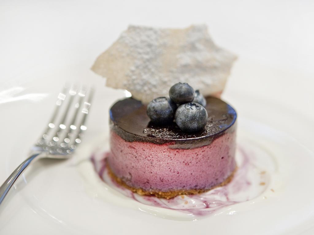 Montcalm Brewery Townhouse Hotel London Exterior photo The photo shows a beautifully plated dessert, which appears to be a round cheesecake or mousse. It has a pinkish-purple filling, topped with a glossy dark chocolate layer. Three fresh blueberries sit on top, adding a pop of color. The dessert is acco