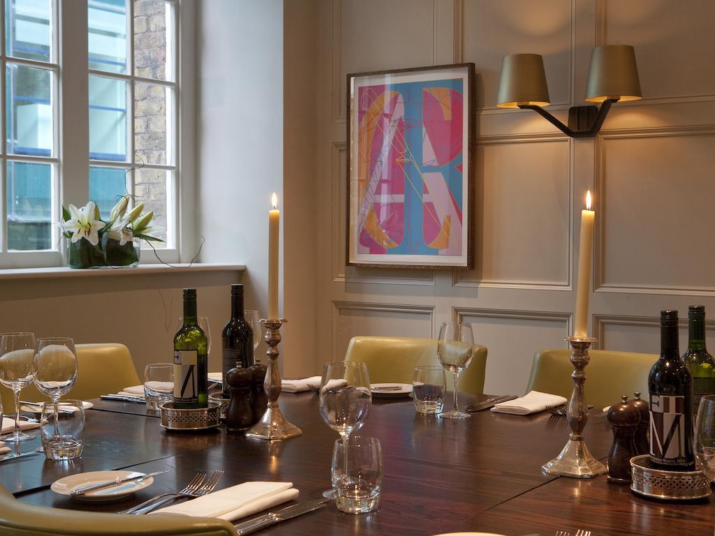 Montcalm Brewery Townhouse Hotel London Exterior photo The photo shows an elegantly set dining room with a large wooden table surrounded by several chairs. The table is adorned with neatly arranged utensils, glasses, and decorative items. There are two tall candlesticks with candles and several bottles o