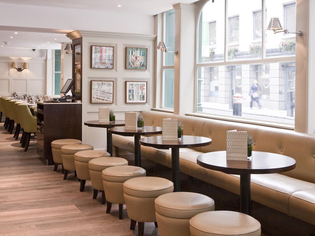 Montcalm Brewery Townhouse Hotel London Exterior photo The photo displays a modern café or restaurant interior. There is a cozy seating area featuring light-colored, upholstered benches along the wall, accompanied by small round tables. The tables are paired with circular stools. The decor includes frame
